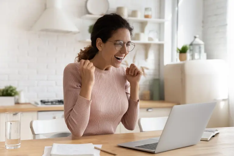 A woman celebrating at her laptop as she finds out she's landed a new job.